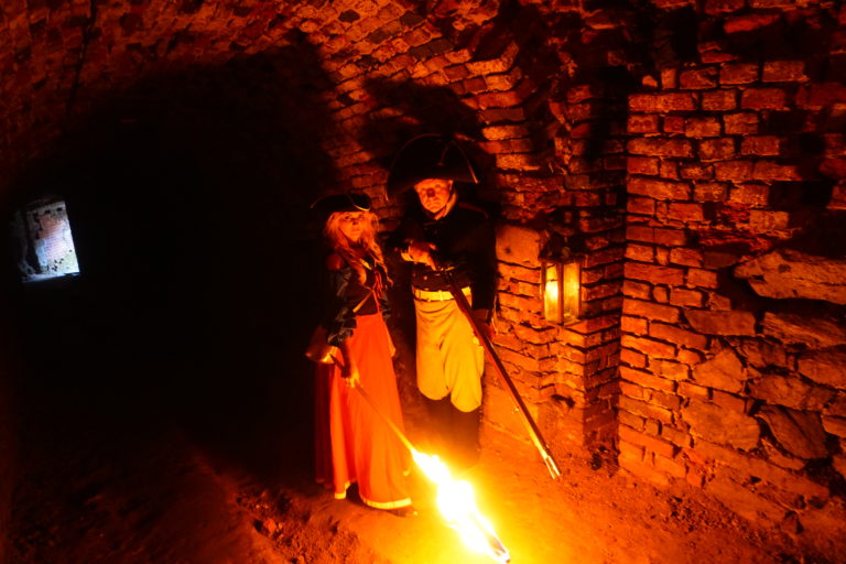 Mężczyzna i kobieta w strojach z epoki w kazamatach Twierdza Srebrna Góra oświetlonych światłem pochodni